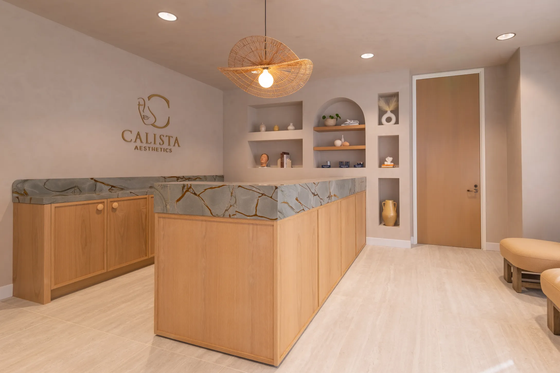 Calista Aesthetics reception area with warm wood, marble accents, and decorative shelving.