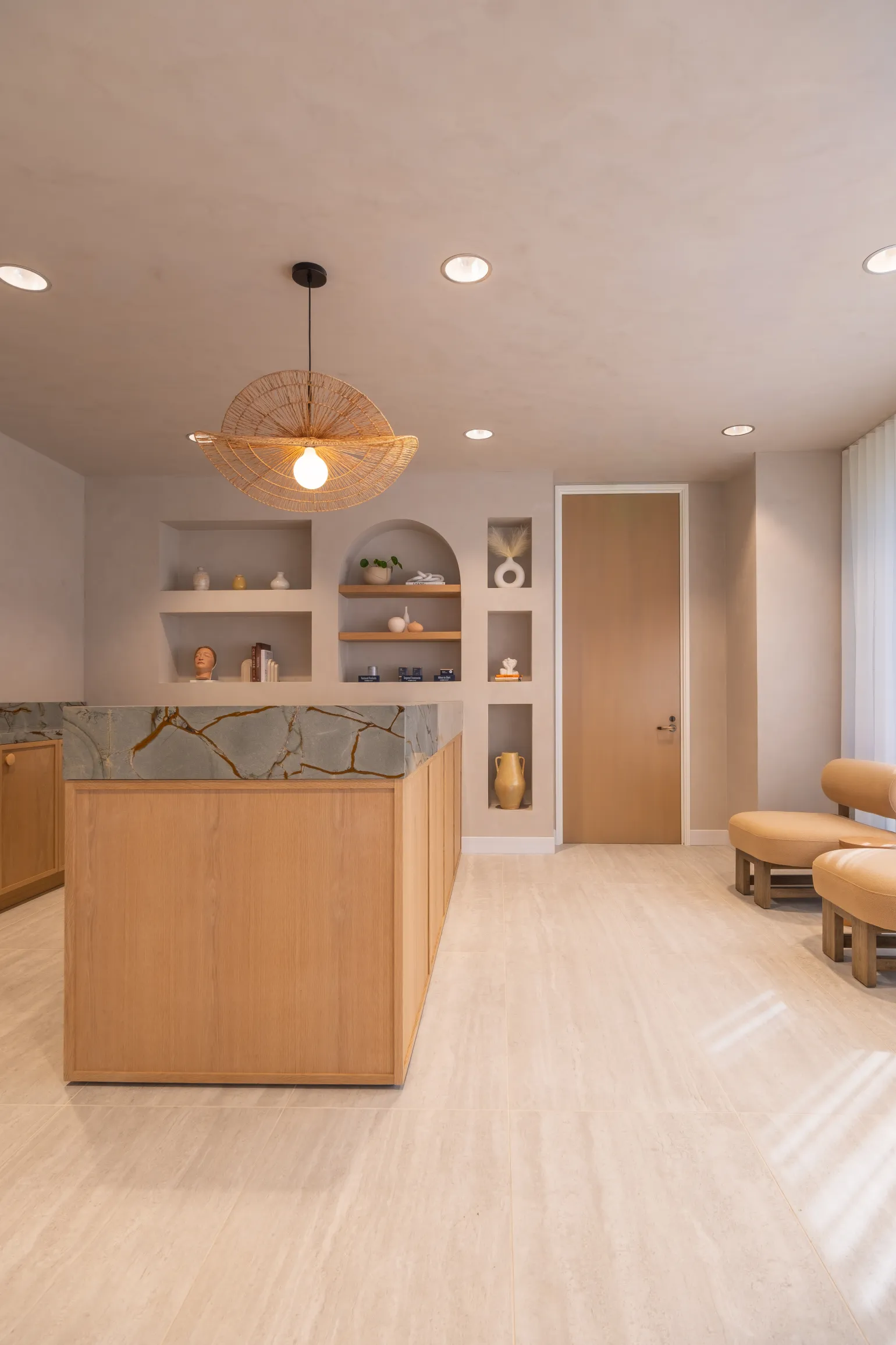 Reception seating area with curved beige chairs, a wooden door, and decorative wall shelving.