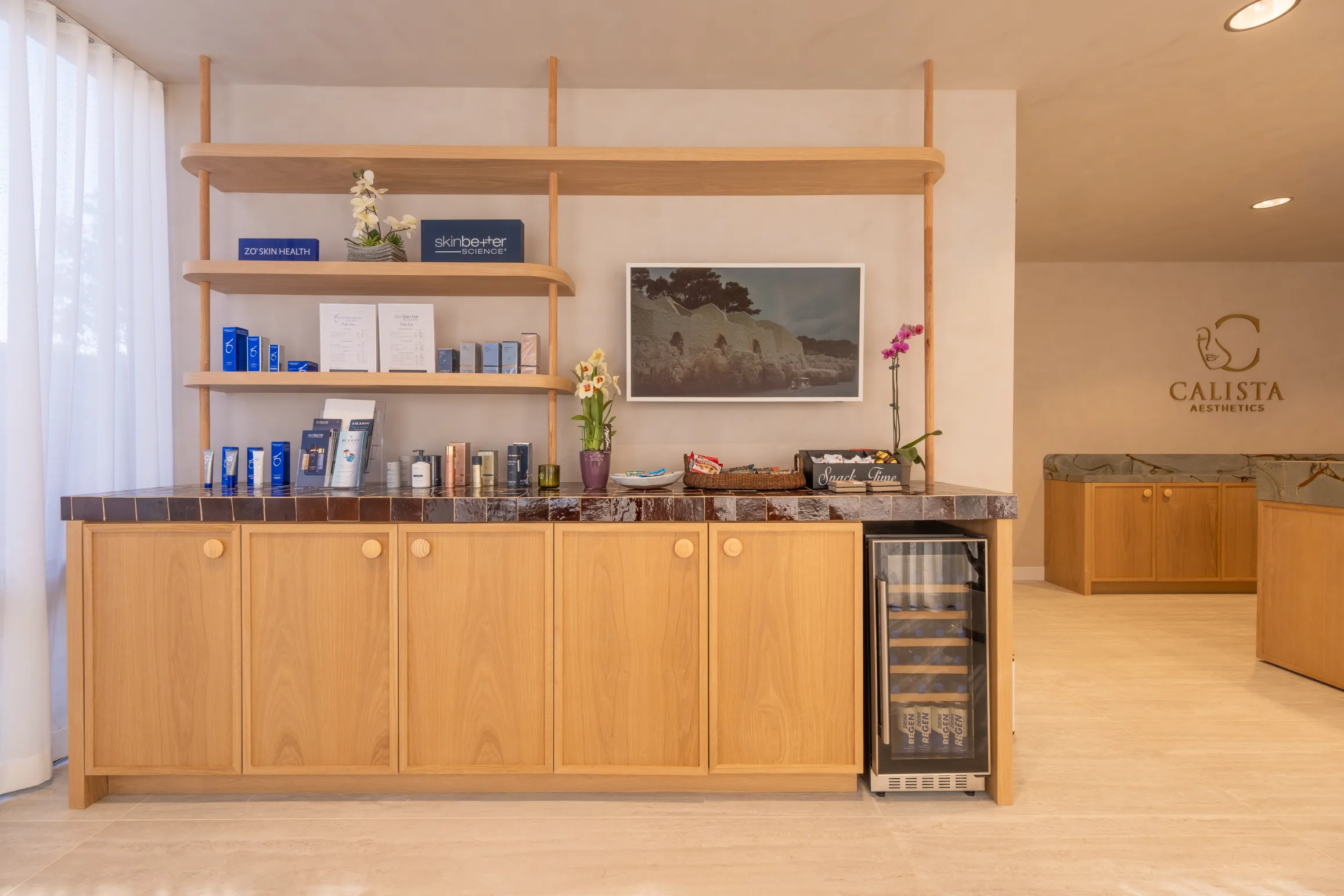 Display shelf with skincare products, flowers, framed art, and a small beverage fridge.